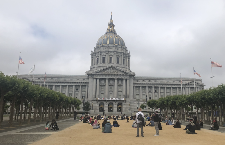 A group of about 100 people sits and meditates in front of City Hall in San Francisco.